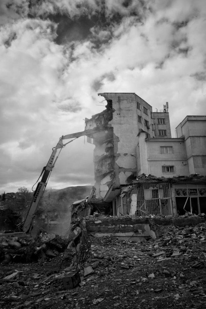 Demolition of a multi-story building with debris and excavator in black and white.