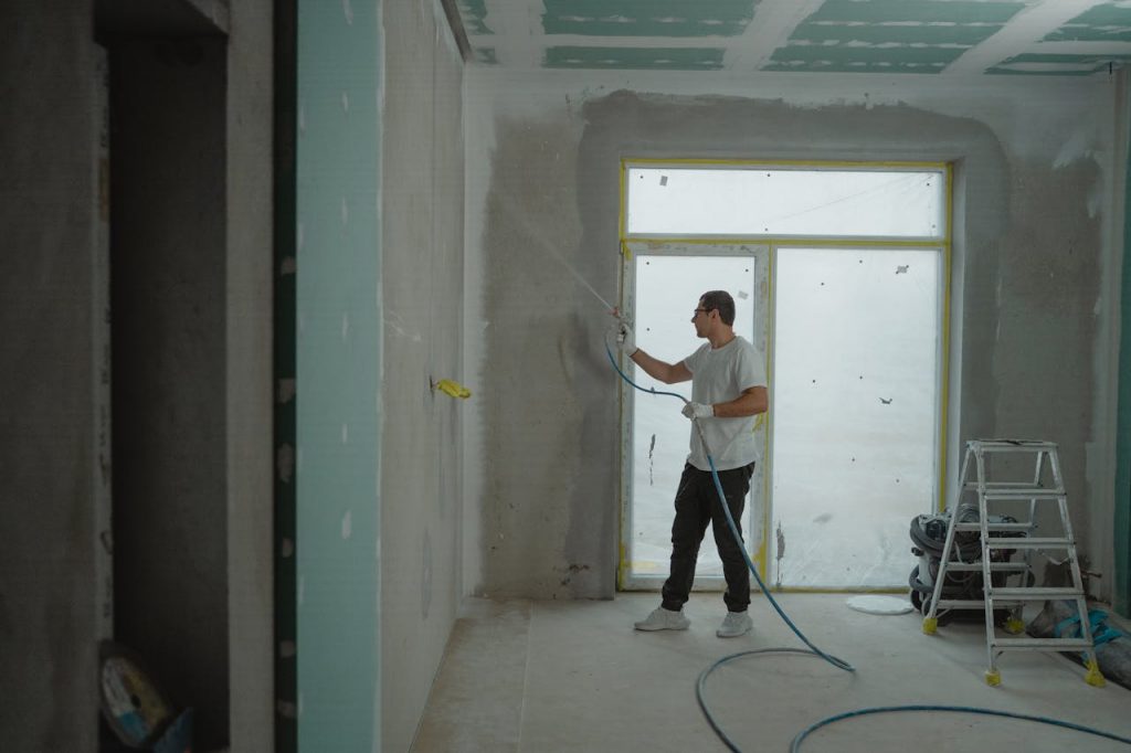 A man sprays paint on a wall while renovating an indoor room with professional equipment.