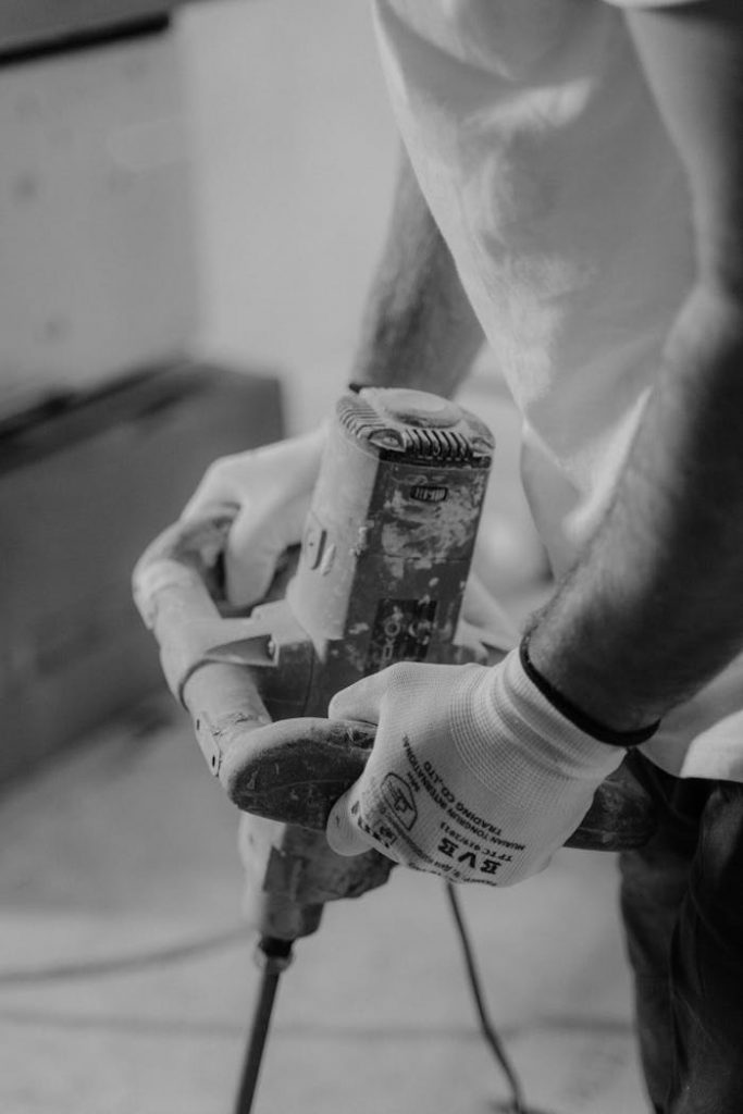 Close-up of a man using a hand drill in a carpentry workshop. Black-and-white image emphasizing craftsmanship.